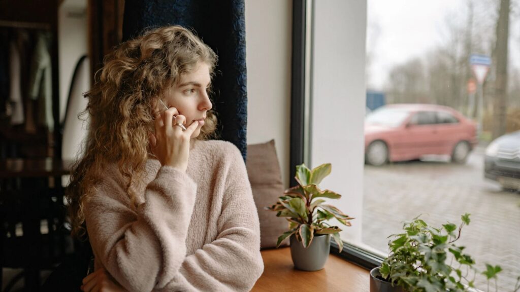 young woman looking out window on cell phone
